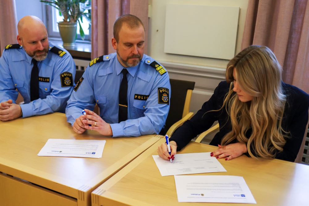 Amanda Lindblad signerar överenskommelsen. David Birgestad och Henrik Keventer från polisen sitter bredvid.